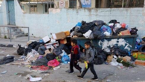 Niños palestinos pasan junto a un montón de basura en el campo de refugiados de Al Jalazone, cerca de Ramala, en Cisjordania, el 25 de enero de 2023. 