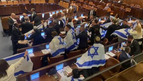 Legisladores de la oposición con banderas israelíes durante el debate sobre la reforma judicial en el pleno de la Knesset. (Ynet) Legisladores de la oposición enarbolan banderas israelíes durante el debate sobre la reforma judicial en el pleno de la Knesset.