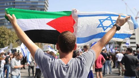Un manifestante ondea banderas palestina e israelí. 