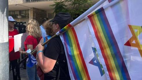 Un manifestante sostiene una bandera israelí y una bandera arco iris durante una manifestación ante el rabinato de Tel Aviv. 