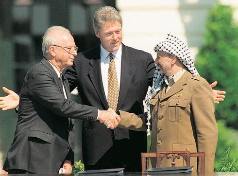 El primer ministro Yitzhak Rabin y el líder palestino Yasser Arafat se dan la mano en la ceremonia de firma de los Acuerdos de Oslo en la Casa Blanca; en el centro: El presidente de EE.UU. Bill Clinton.