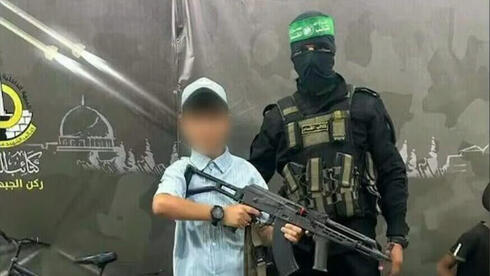 Un niño de Gaza sosteniendo un rifle junto a un terrorista de Hamás 